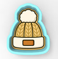 A cookie cutter in the shape of a winter hat with a pom pom on top.