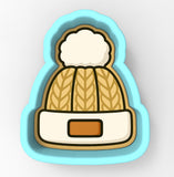 A cookie cutter in the shape of a winter hat with a pom pom on top.