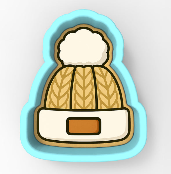 A cookie cutter in the shape of a winter hat with a pom pom on top.