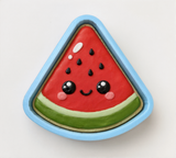 A cookie shaped like a slice of watermelon with a smiling face and black dots on top.