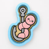 A cookie cutter in the shape of a cartoon fish with a pink fish-like creature on it.