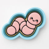 A cookie cutter in the shape of a cute pink caterpillar with a smiling face.