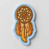 A cookie cutter in the shape of a dreamcatcher, with a brown wooden frame and three orange feathers.