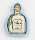 A blue cookie cutter shaped like a bottle of tequila, with a label that reads "100% AGVEC BLANCO".