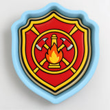 A shield-shaped cookie cutter with a red and yellow design featuring a fire extinguisher and flames.