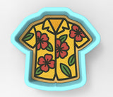 A cookie cutter in the shape of a yellow Hawaiian shirt with red flowers.