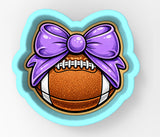 A cookie cutter in the shape of a football with a purple bow on top.