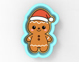 A cookie cutter in the shape of a gingerbread man wearing a Santa hat.