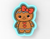 A cookie cutter in the shape of a gingerbread girl with a bow on her head and hearts on her chest.
