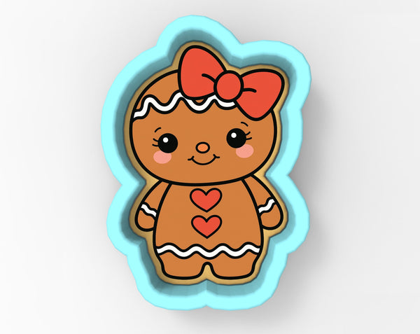 A cookie cutter in the shape of a gingerbread girl with a bow on her head and hearts on her chest.
