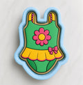 A cookie cutter in the shape of a baby's swimsuit, with a flower design on the front.