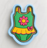 A cookie cutter in the shape of a baby's swimsuit, with a flower design on the front.