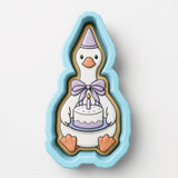 A cookie cutter in the shape of a duck holding a birthday cake.