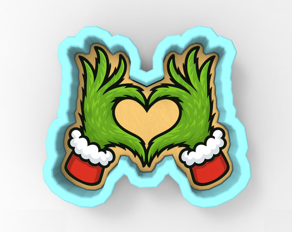 A cookie cutter in the shape of a heart, with two green hands wearing Santa hats on either side of the heart.