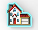 A cookie cutter in the shape of a house with a red door and a garage.