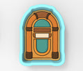 A jukebox cookie cutter in the shape of a jukebox, with a wooden frame and a turquoise background.