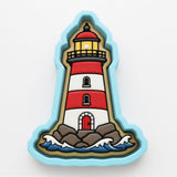 A cookie cutter shaped like a lighthouse, with a red and white striped body, a yellow light at the top, and a red door at the bottom.
