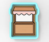 A blue cookie cutter shaped like a wooden stall or booth with a white interior.