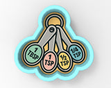 A blue and yellow cookie cutter with four measuring spoons labeled with different amounts of ingredients, such as 1 teaspoon, 1/4 teaspoon, 1 tablespoon, and 1/2 tablespoon.