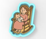 A woman is sitting in a rocking chair, holding a baby wrapped in a blanket.