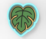 A heart-shaped cookie cutter with a green leaf design on it.