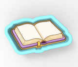 An open book with blank pages, placed on a blue tray or cookie cutter.