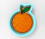 An orange-colored cookie cutter with a leaf attached, set against a plain white background.