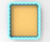 A blue, square-shaped baking pan with a scalloped edge, containing a yellow substance, likely a batter or dough.