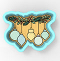 A cookie cutter-shaped design with a festive arrangement of Christmas ornaments hanging from a branch.