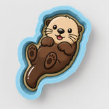 A cartoon image of an otter in a blue cookie cutter.