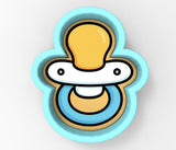 A baby pacifier cookie cutter in the shape of a smiling baby's face.
