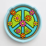 A colorful peace sign made of various colored flowers, including pink, orange, yellow, and green, arranged in a circular pattern.