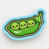 A cookie cutter in the shape of a green pea pod with three peas inside, each with a smiling face.