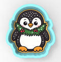 A cute cartoon penguin cookie cutter with a festive wreath around its neck.
