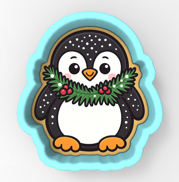 A cute cartoon penguin cookie cutter with a festive wreath around its neck.