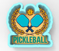 a logo for a sport called "Pickleball". The logo consists of two blue paddles crossed in an X shape, with a yellow ball above them, all set against a light blue background. The word "Pickleball" is prominently displayed below the logo.