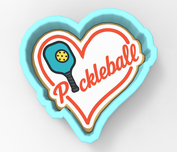 A heart-shaped cookie cutter with the word "Pickleball" written on it, along with a tennis racket icon.