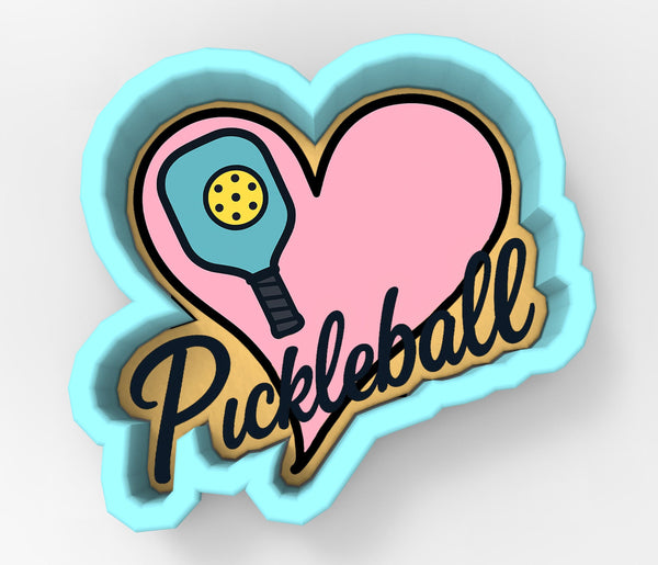 A heart-shaped cookie cutter with a paddleball symbol and the word "Pickleball" written on it.