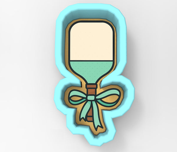 A cookie cutter in the shape of a tennis racket with a bow around the handle.