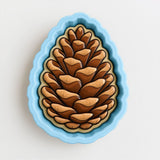 A blue ceramic dish containing a detailed illustration of a pine cone.