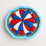 A blue cookie cutter with a colorful design of red, white, and blue shapes on it.