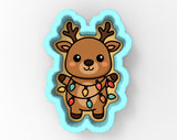 A cartoon reindeer cookie cutter with a string of colorful Christmas lights wrapped around it.