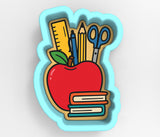 A cookie cutter in the shape of an apple, filled with school supplies such as pencils, scissors, and books.