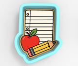 A cookie cutter in the shape of a school-related item, such as a pencil and an apple, with a blank lined paper sheet.