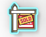 a cookie cutter-shaped sign with a white post and a red and yellow "SOLD" sign attached to it.