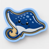 A blue and white cartoon-style stingray with a smiling face and large eyes is depicted in the image.