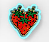 A heart-shaped cookie cutter with three red strawberries on it.