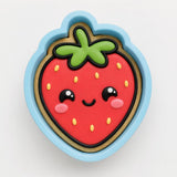A cookie cutter shaped like a strawberry with a smiling face and green stem.