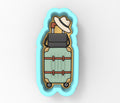 A blue cookie cutter shaped like a suitcase with a hat on top.
