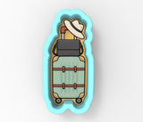 A blue cookie cutter shaped like a suitcase with a hat on top.